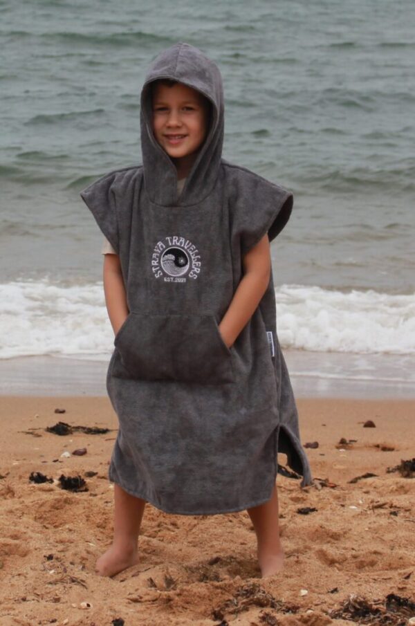 A young boy is standing on the beach wearing a towel.